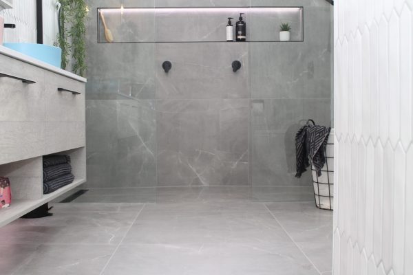 Bathroom with walk in double shower, large shower niche with lighting with large format grey floor tiles and feature wall